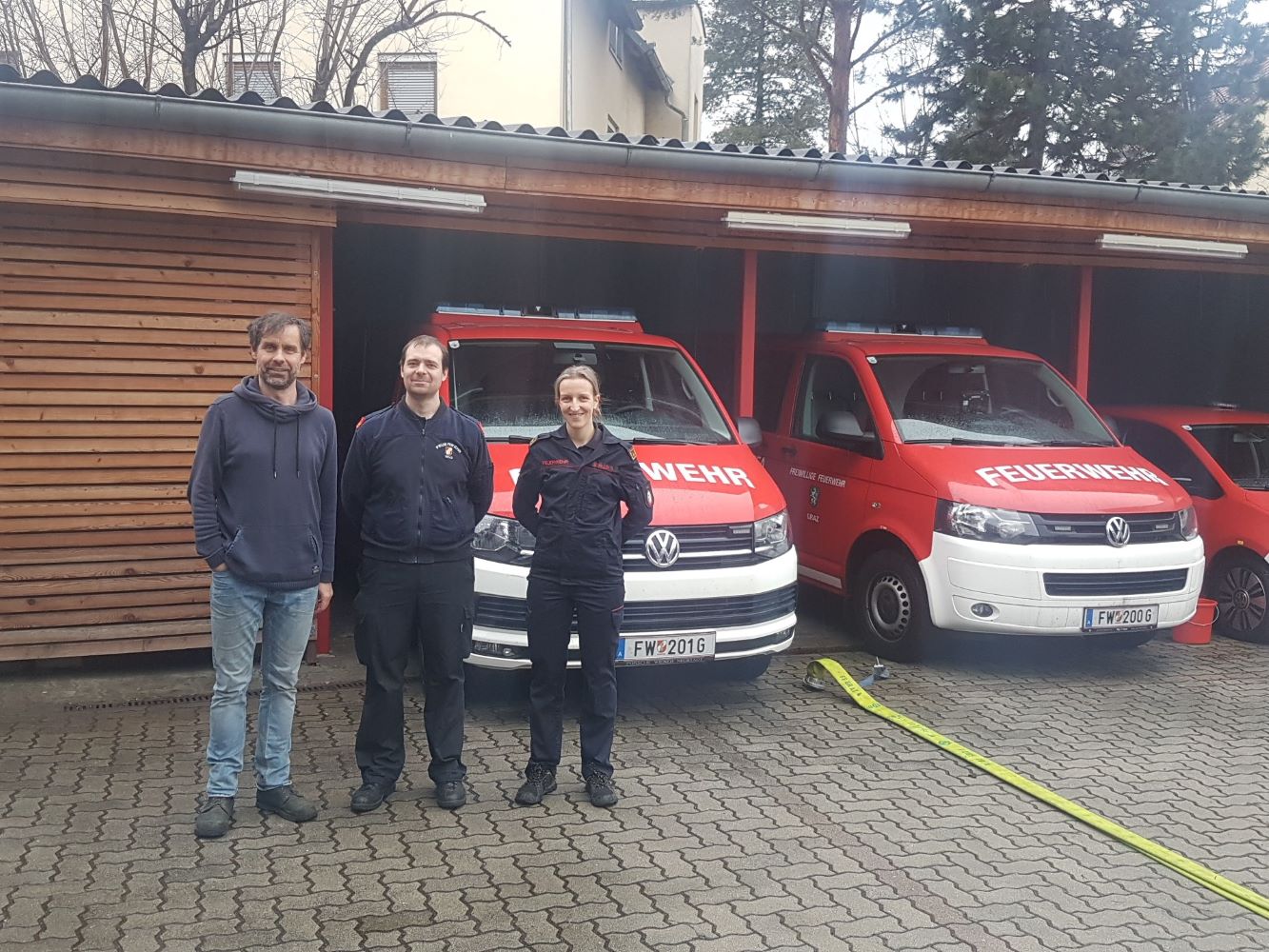 Zu sehen sind: drei Menschen vor zwei Feuerwehrautos.