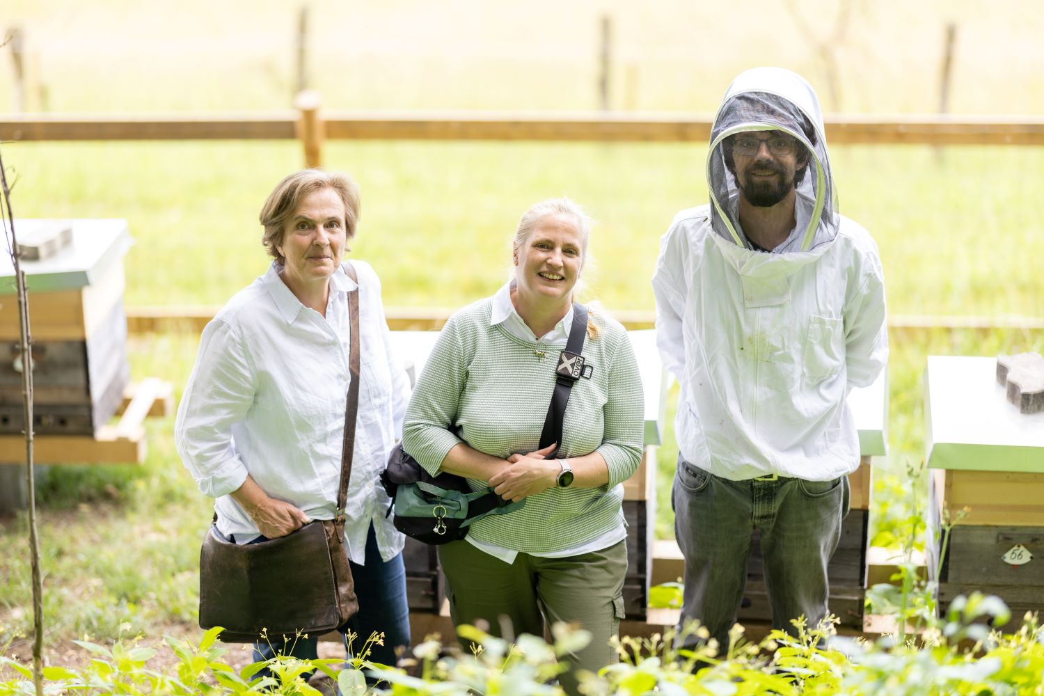 Zu sehen sind: drei Personen vor Bienenstöcken
